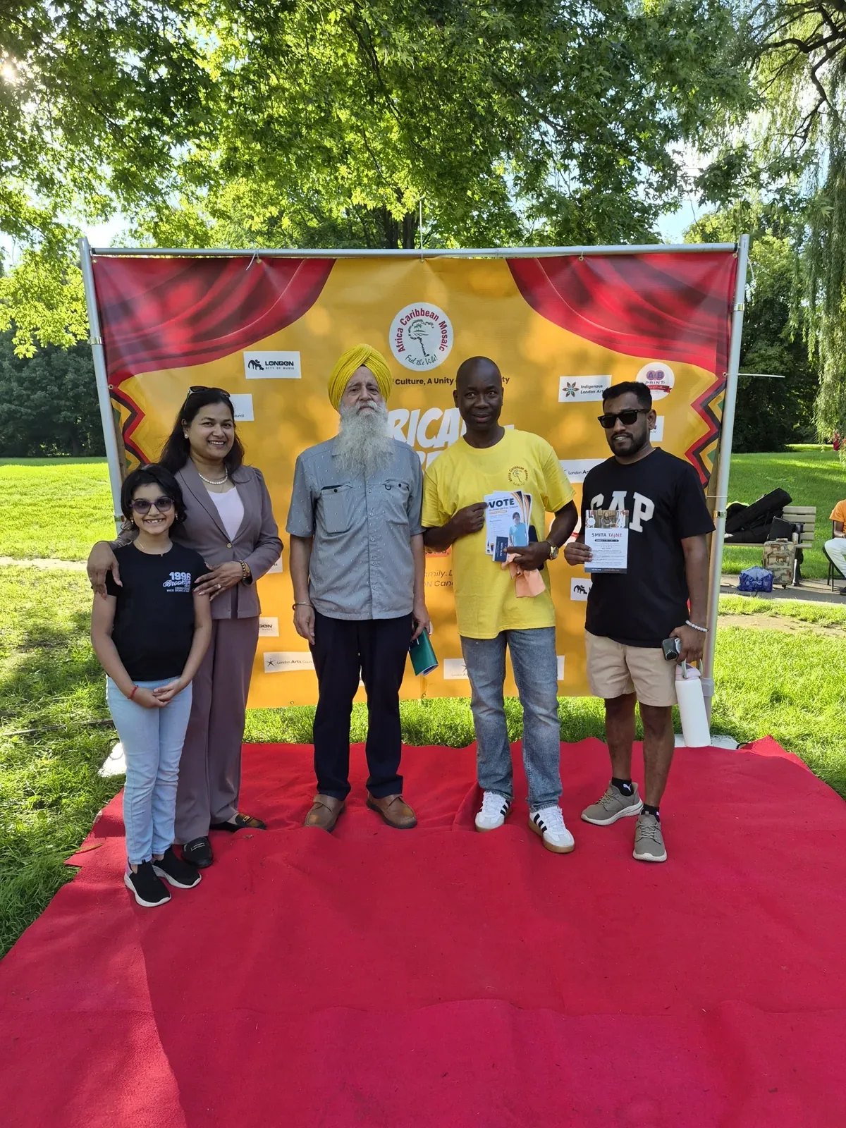Gurinder Pal Singh with community members in front of the African-Caribbean Mosaic banner at the festival in London, Ontario